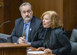 Elizabeth Wefel sits at the testifiers' table and speaks into a microphone to someone out of view. Representative Hansen sits next to her.